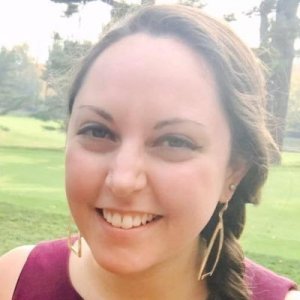 Image of a girl in her twenties with long earrings and long brown hair smiling at the camera.