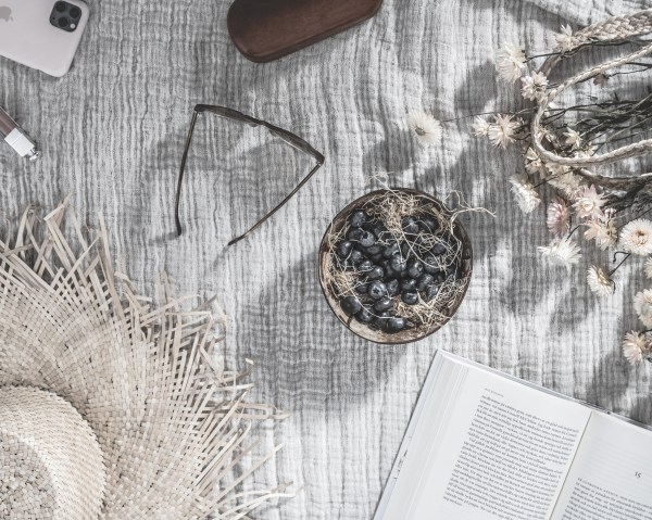 A top-down photograph. Atop a gray and white table cloth lays a straw hat in the bottom left-hand corner, an open hardcover book in the bottom right-hand corner,