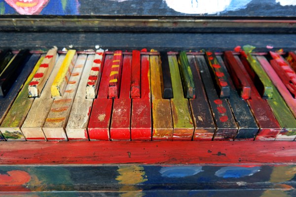 A close-up of piano keys besmeared with all colors of paint.